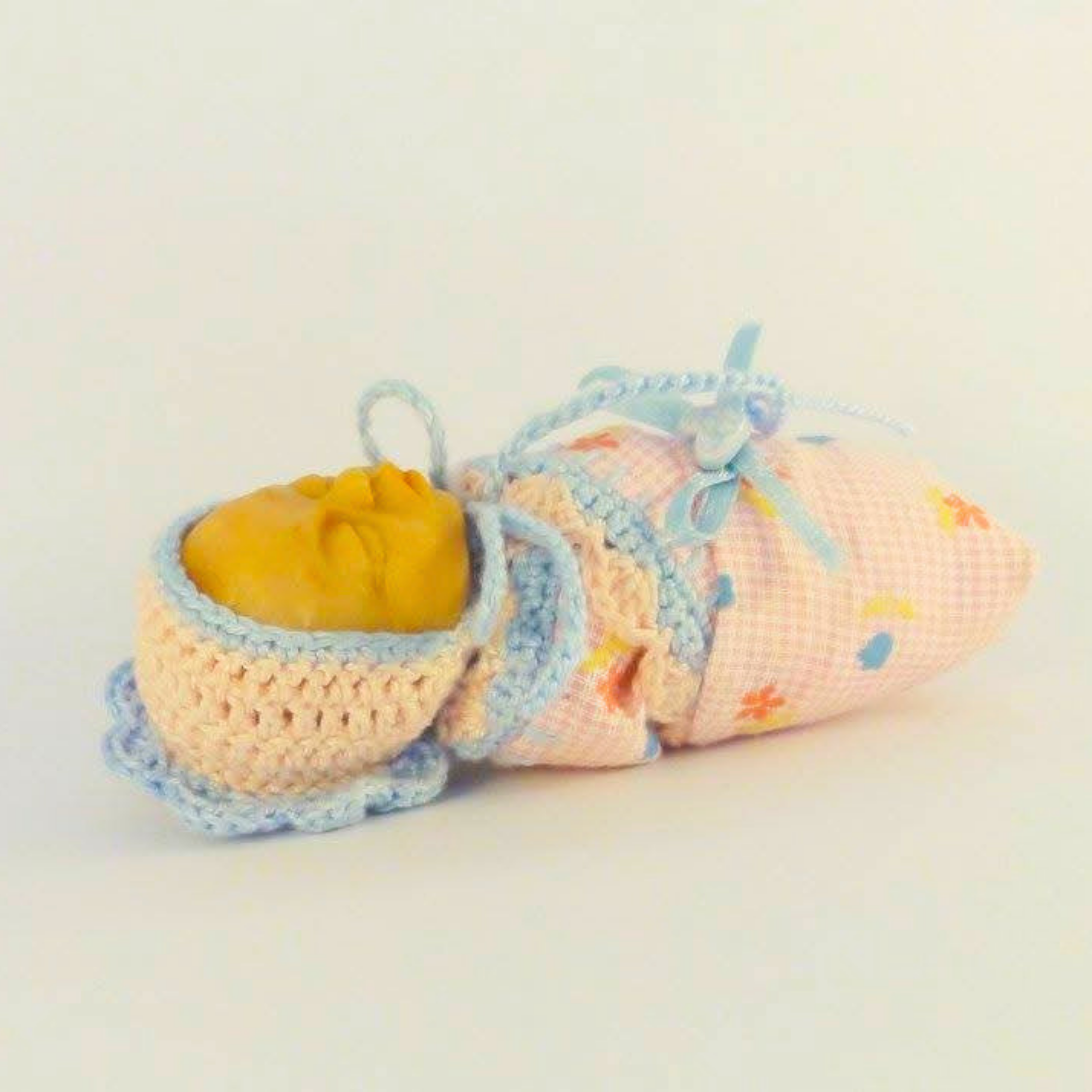 Tiny sleeping polymer clay pocket doll wrapped in a pink floral swaddle and wearing a pale blue and pink crocheted bonnet.