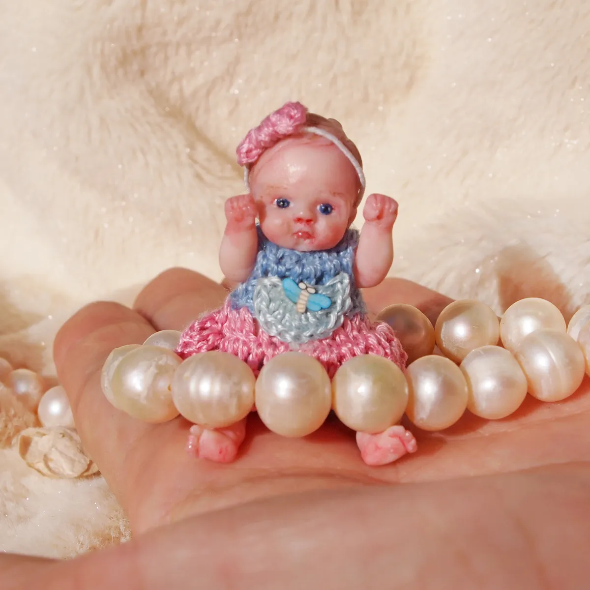 Charming OOAK miniature baby doll in blue crocheted dress with tiny bow detail, surrounded by elegant pearl beads - by Mini Baby Dolls