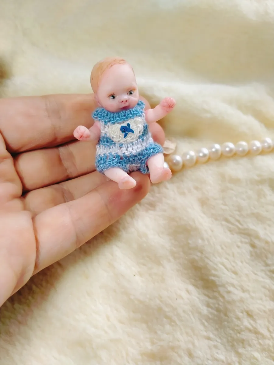 Cheerful OOAK miniature baby doll in blue crocheted romper with teddy bear emblem, displayed with pearl beads - by Mini Baby Dolls