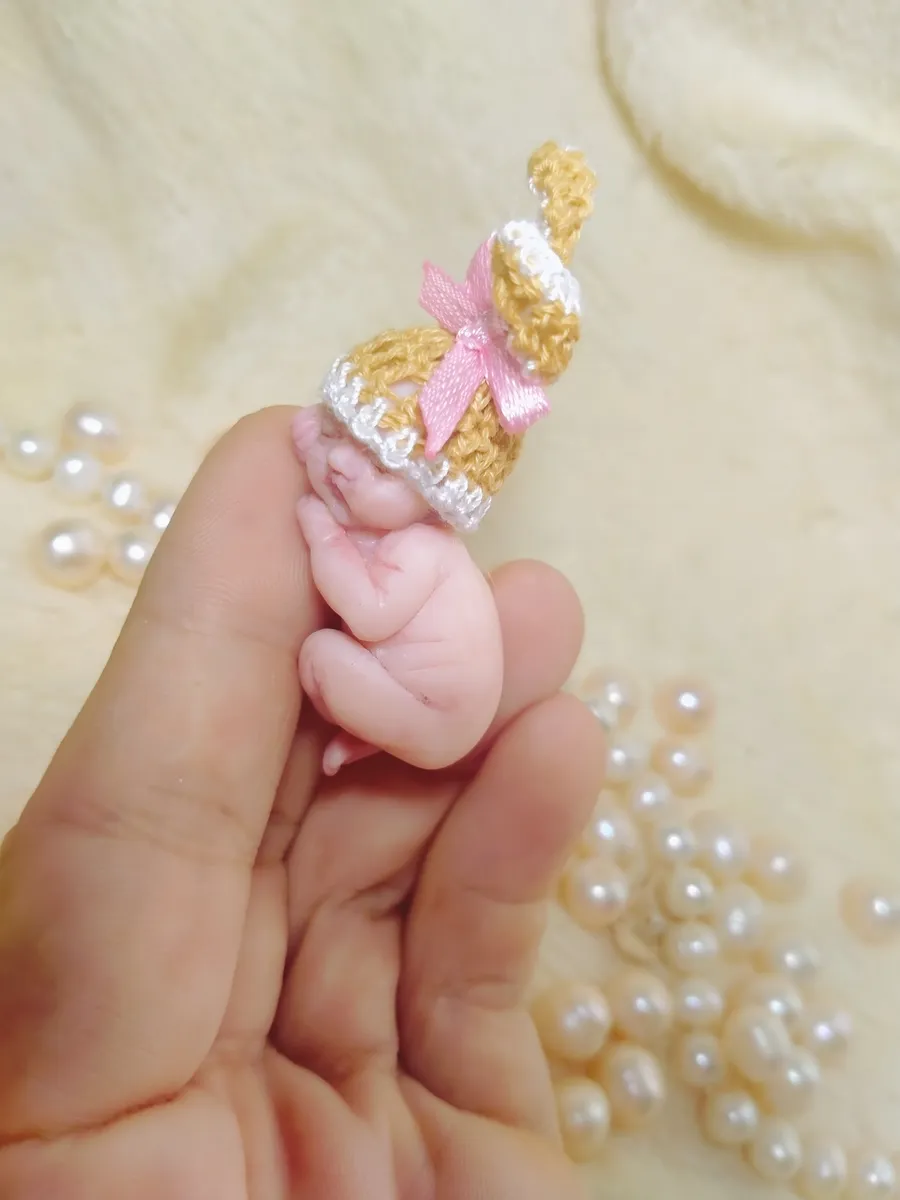 OOAK miniature baby doll in golden yellow crocheted outfit with pink bow accent, displayed in palm with pearl beads - by Mini Baby Dolls