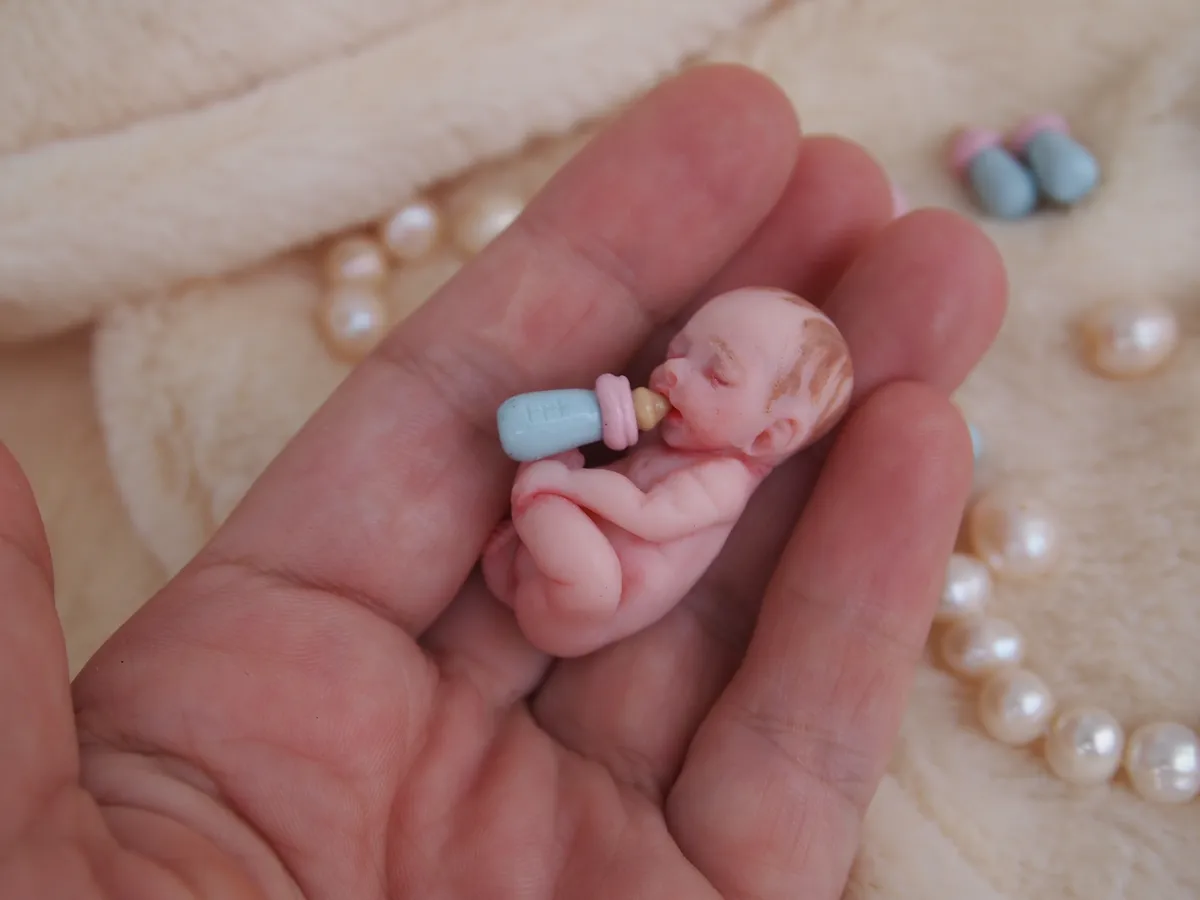 Sleeping OOAK miniature baby doll hugging tiny blue baby bottle accessory, cradled in palm with pearl beads - by Mini Baby Dolls