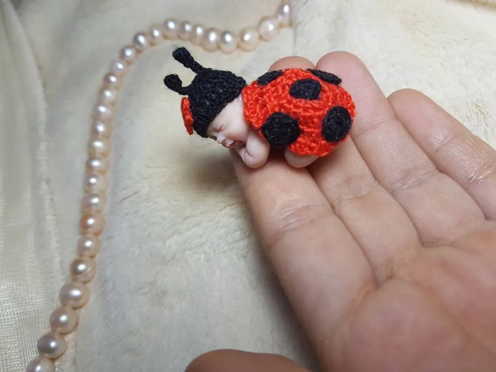 Adorable OOAK miniature baby doll in red and orange crocheted ladybug costume with black spots, held gently in palm - by Mini Baby Dolls