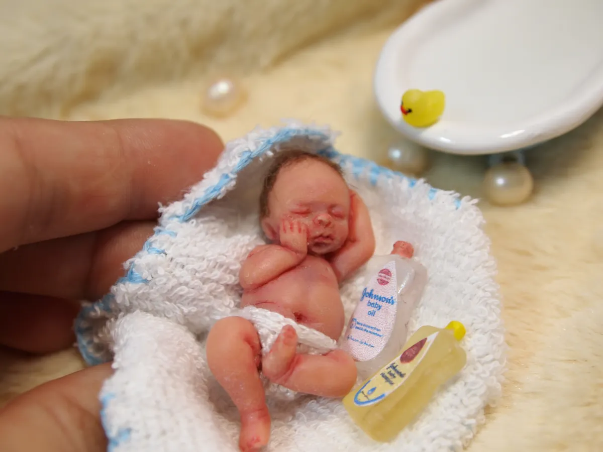 Sleeping OOAK miniature baby doll on blue crocheted blanket with miniature bath accessories - rubber duck, shampoo, and lotion bottles - by Mini Baby Dolls