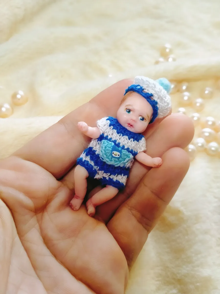 Cheerful OOAK miniature baby doll in blue and white crocheted sweater with matching headband, displayed in palm with pearl beads - by Mini Baby Dolls