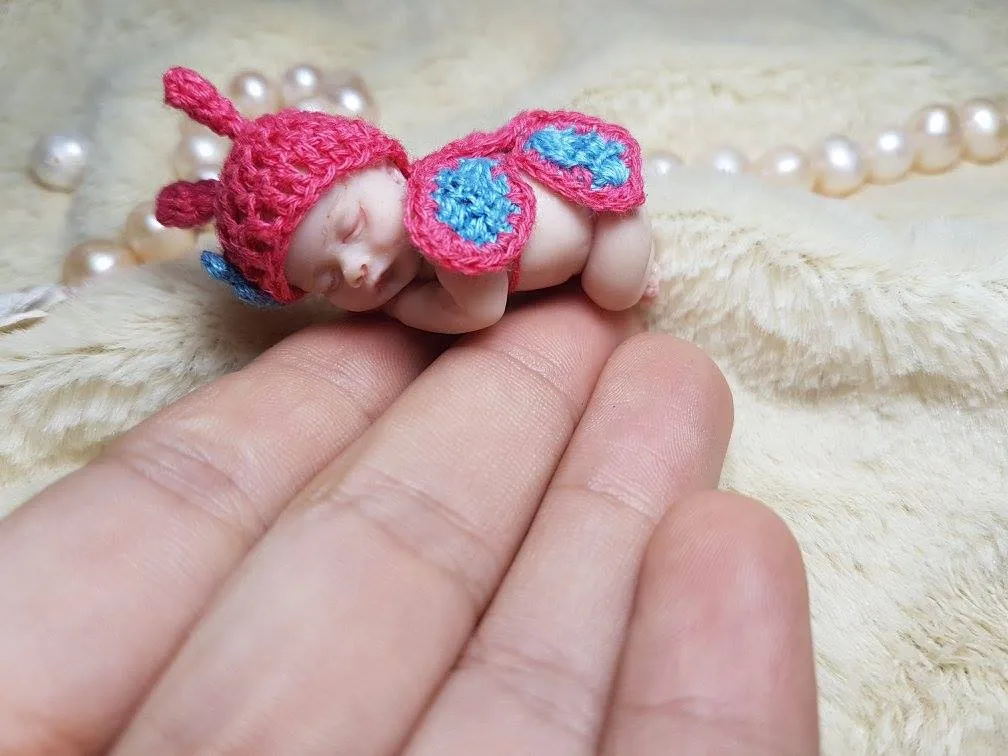 Magical OOAK miniature butterfly baby doll in pink crocheted costume with blue wings, displayed in palm with pearl beads - by Mini Baby Dolls