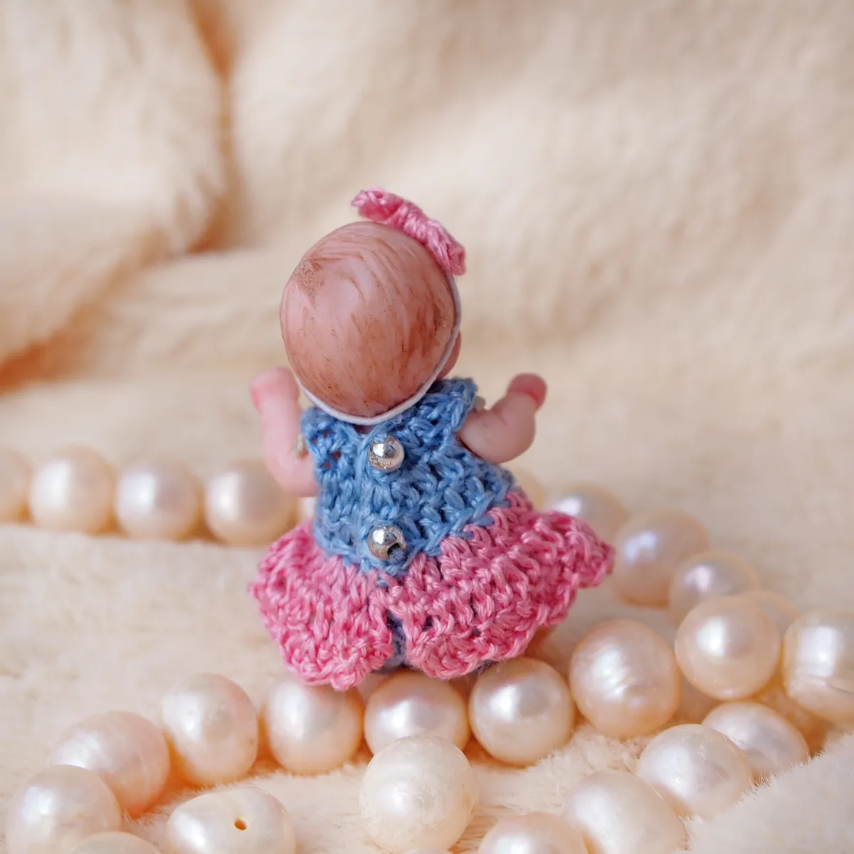 Character OOAK miniature polymer clay doll with expressive older baby face, wearing a blue crocheted dress over pink skirt, surrounded by pearl beads - by Mini Baby Dolls