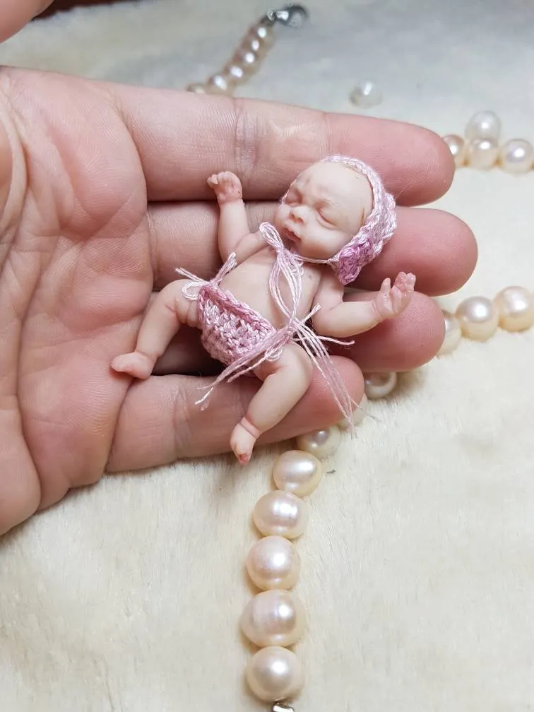 Delicate OOAK miniature baby doll in pink crocheted outfit with ribbon ties, displayed in palm with pearl beads - by Mini Baby Dolls