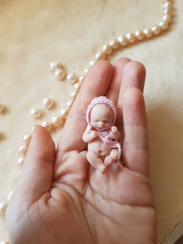 Delicate OOAK miniature baby doll in soft pink crocheted outfit with matching bonnet, sleeping peacefully in palm showing tiny realistic scale - by Mini Baby Dolls