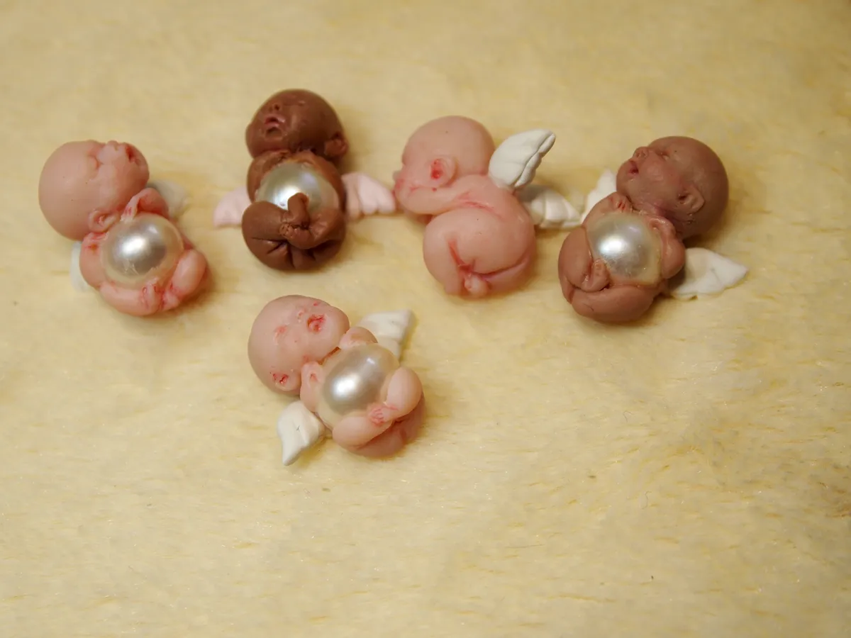 Collection of OOAK miniature baby dolls with diverse skin tones, each holding pearl beads, displayed on cream blanket - by Mini Baby Dolls