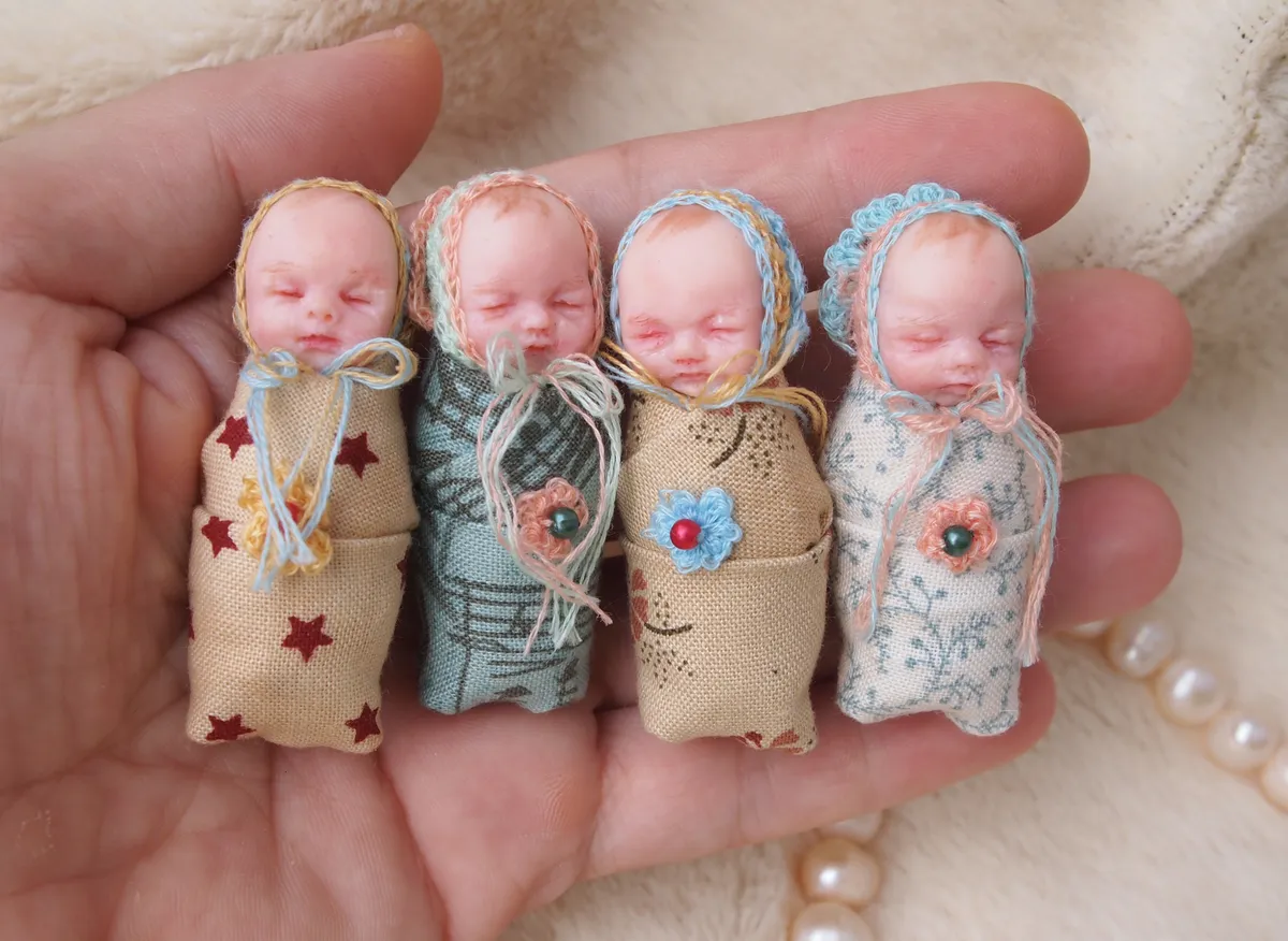 Four adorable OOAK miniature swaddled baby dolls in handmade knitted blankets with matching bonnets in cream, teal, tan and floral patterns, displayed together in palm - by Mini Baby Dolls