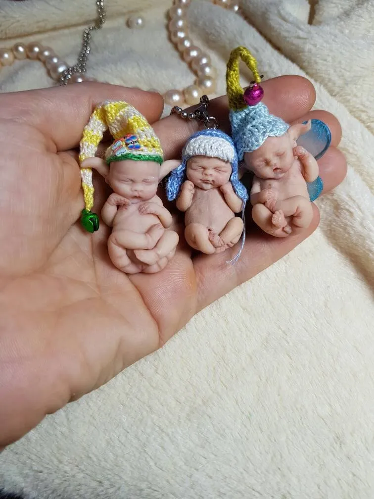 Four OOAK miniature baby dolls with colorful striped crocheted hats and tiny pacifiers, displayed together in palm as adorable keychain collectibles - by Mini Baby Dolls