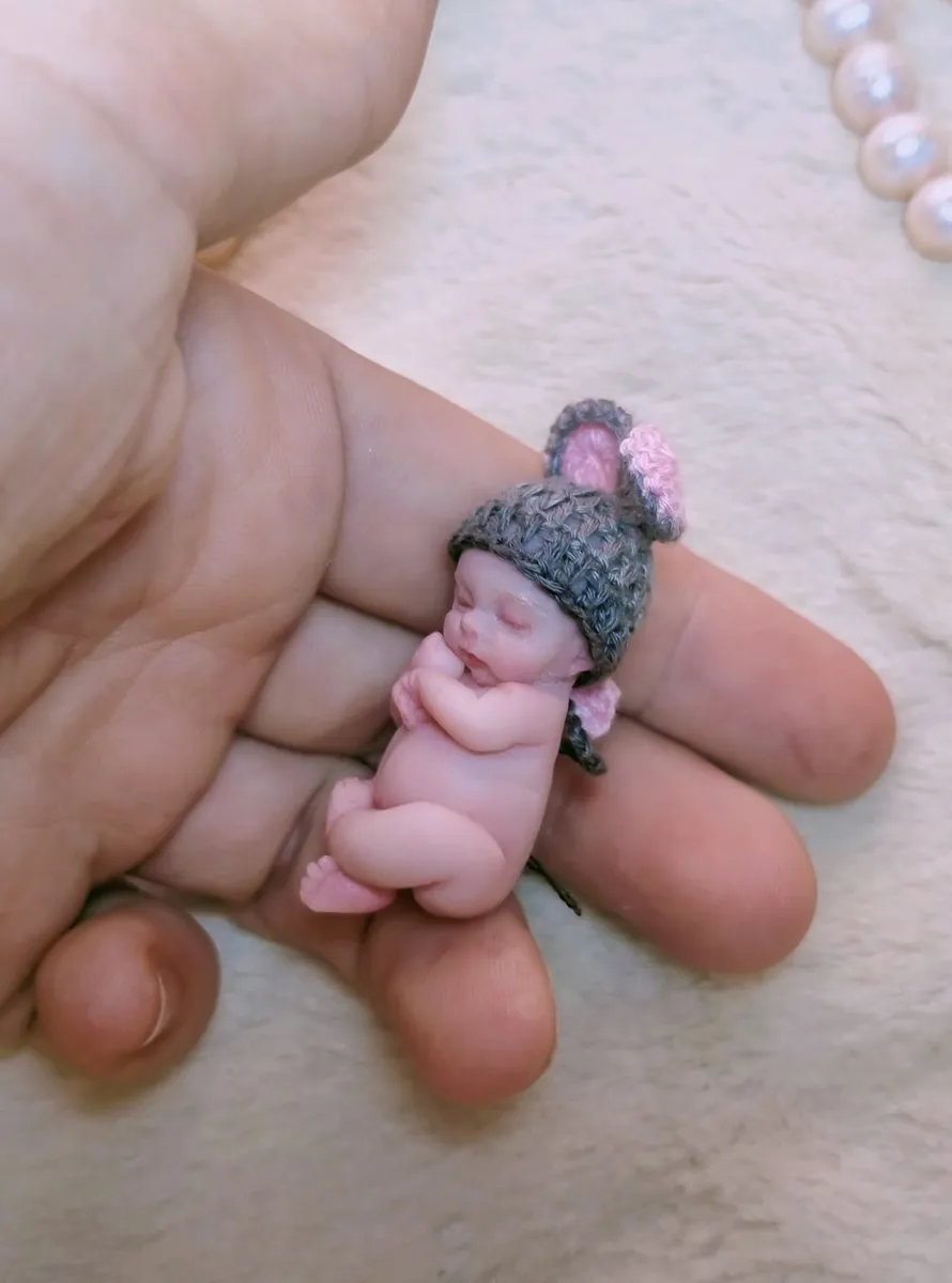 Sleeping OOAK miniature baby doll in grey crocheted mouse-ear hat with fluffy pom poms, held gently in palm with pearl beads - by Mini Baby Dolls