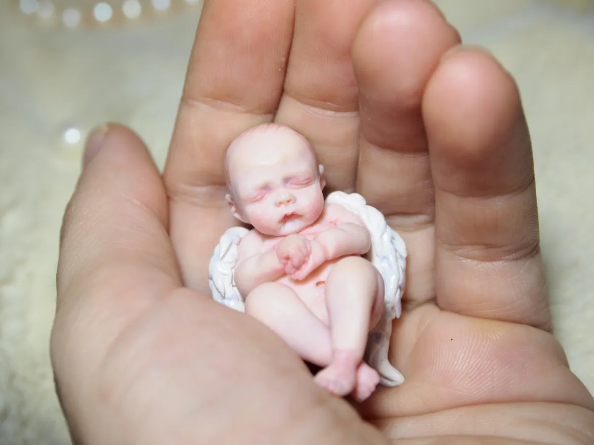 Hyper-realistic OOAK polymer clay newborn baby doll with delicate lifelike skin tones and peaceful sleeping expression, cradled gently in palm showcasing incredible miniature scale - by Mini Baby Dolls