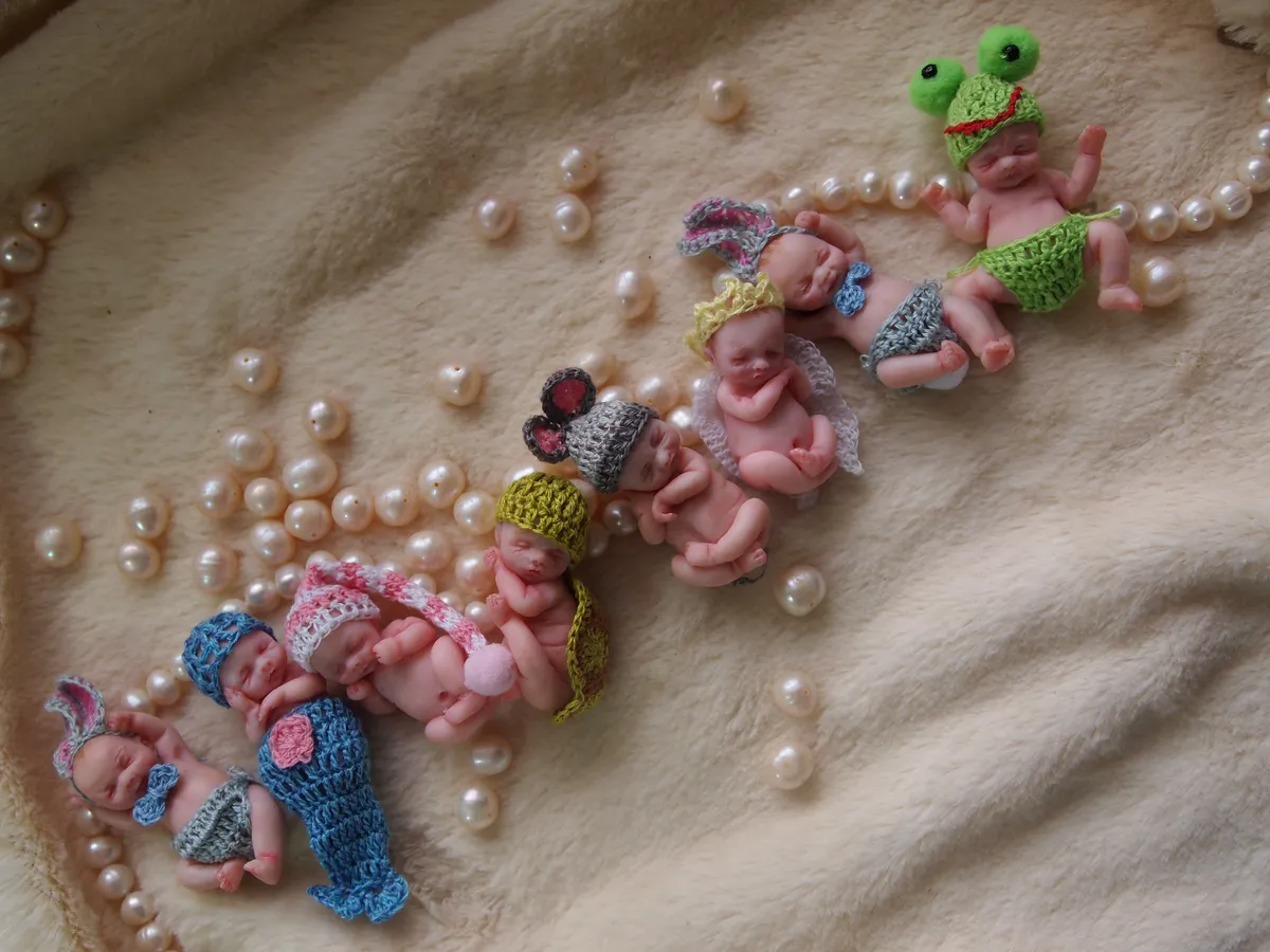 Large collection of colorful OOAK miniature baby dolls in various crocheted costumes displayed together with tiny sculpted frog toys - by Mini Baby Dolls