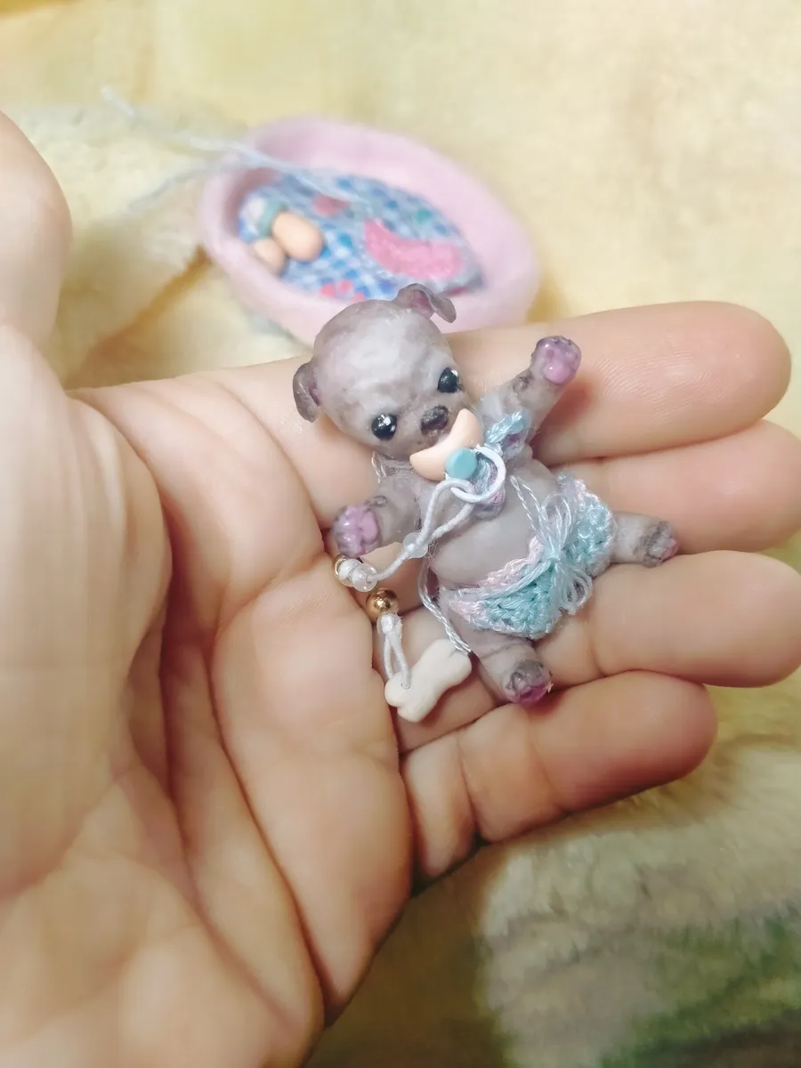 Adorable OOAK miniature mouse/teddy figurine with pacifier and blue crocheted outfit, displayed in palm with pink carrier accessory - by Mini Baby Dolls