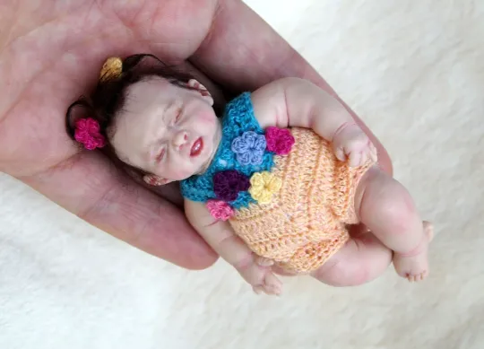 Sleeping OOAK miniature baby doll in orange crocheted romper outfit with colorful ruffles, held gently in palm - by Mini Baby Dolls