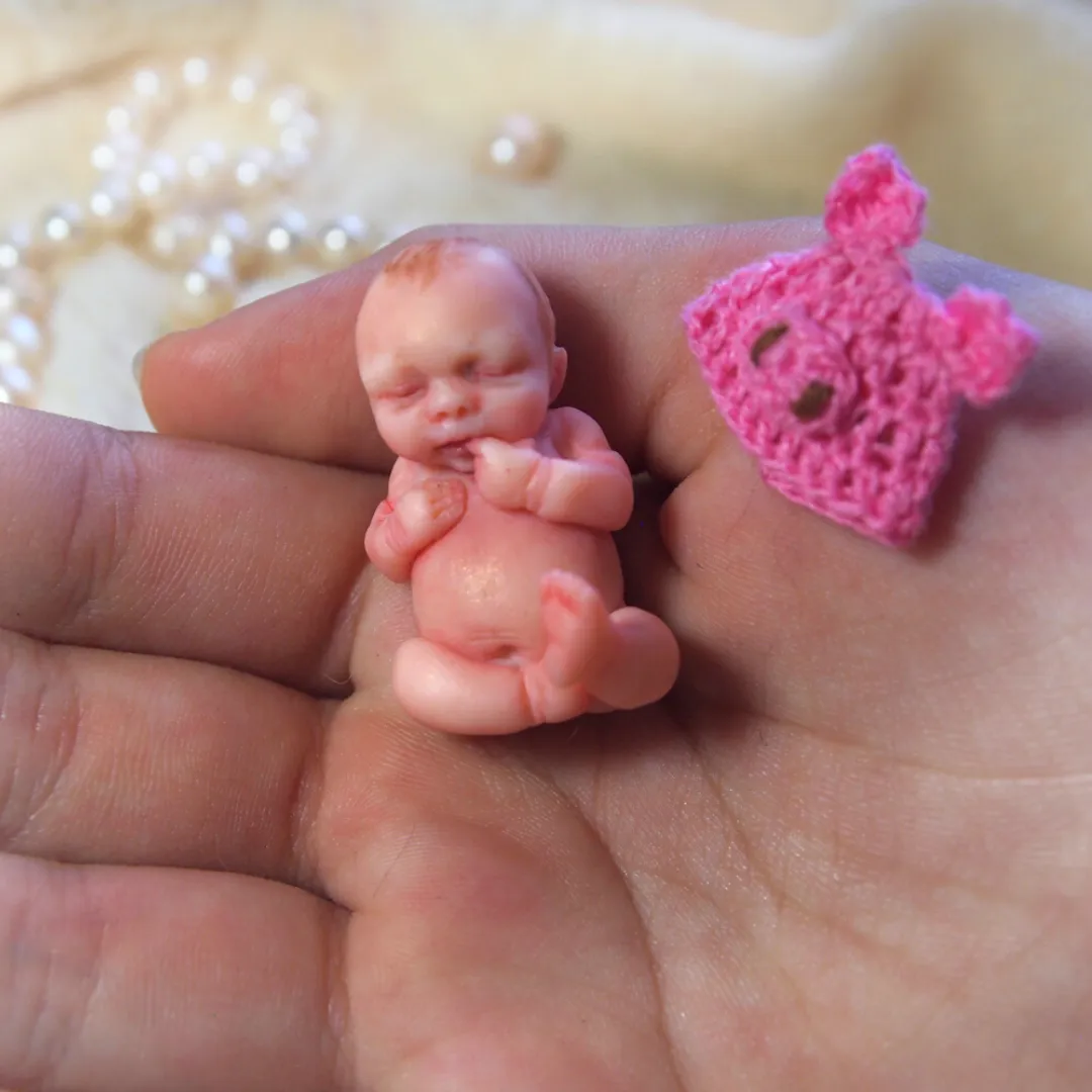 Peaceful sleeping OOAK miniature baby doll with a tiny pink crocheted heart beside it, displayed in palm with pearl beads - by Mini Baby Dolls