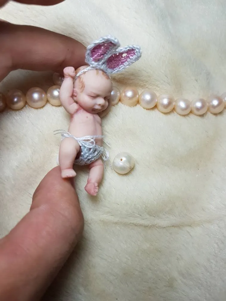 Playful OOAK miniature baby doll wearing lavender bunny ear headband and matching outfit, displayed with pearl beads - by Mini Baby Dolls