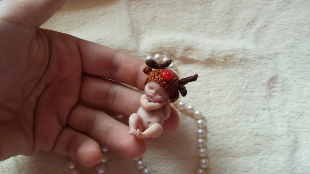 Cute OOAK miniature baby doll with brown reindeer antlers accessory, posing in palm with pearl beads and soft lighting - by Mini Baby Dolls