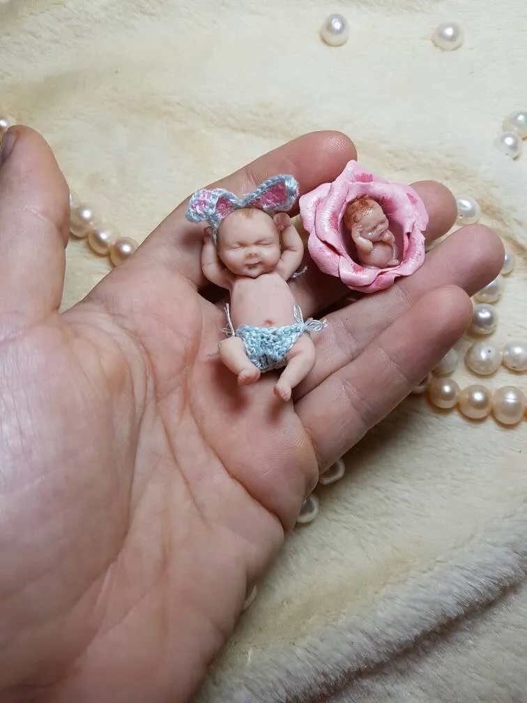 Sleeping OOAK miniature baby doll in blue crocheted outfit with a delicate pink rose flower beside it, displayed with pearl beads - by Mini Baby Dolls