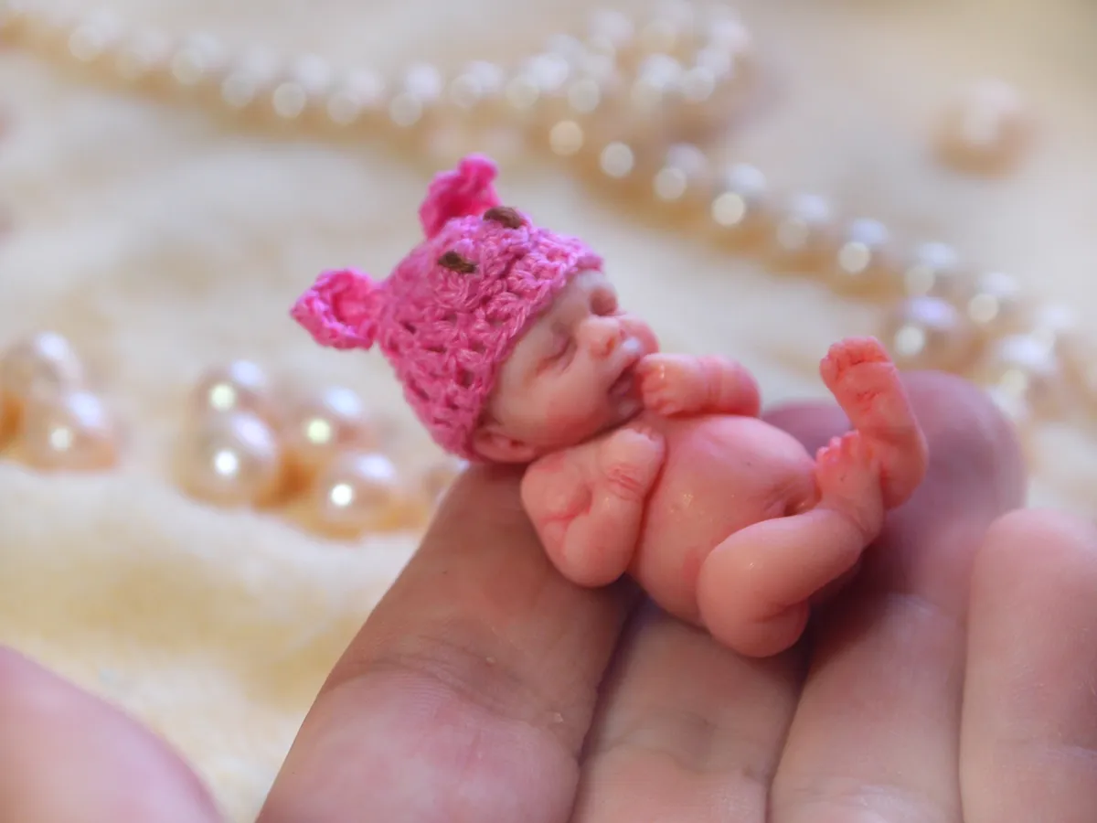 Sleeping OOAK polymer clay miniature baby doll cuddling a tiny handmade pink crocheted teddy bear, displayed with pearl beads - by Mini Baby Dolls