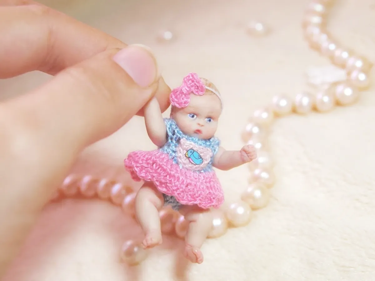 Adorable OOAK miniature baby doll in pink crocheted tutu dress with matching pink headband, posed playfully with pearl beads - by Mini Baby Dolls