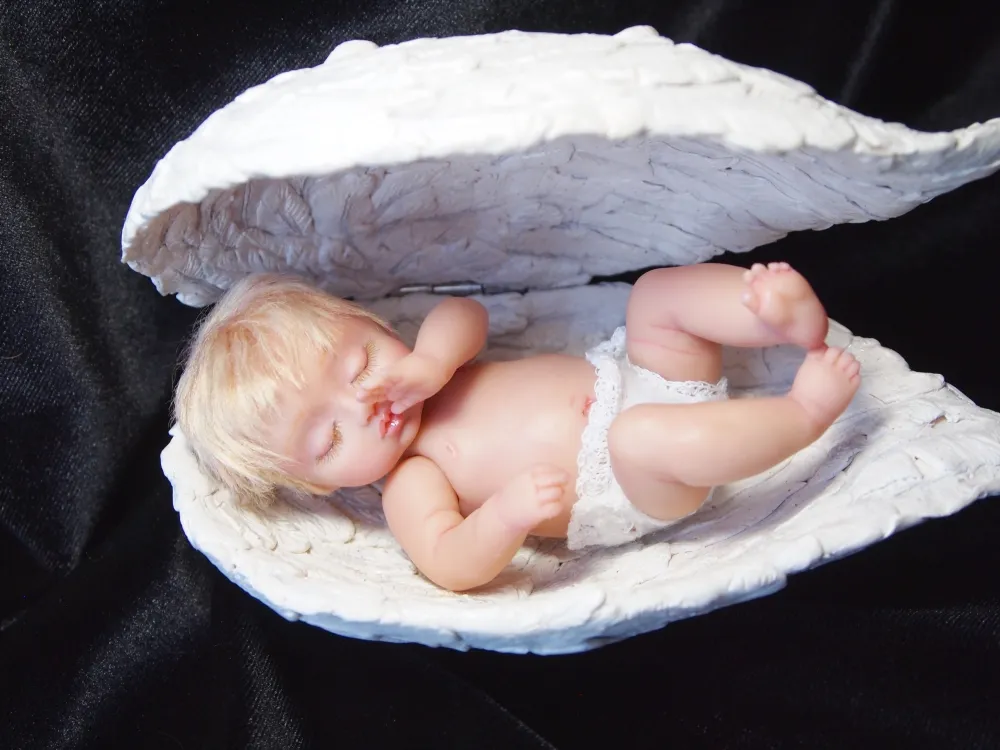 Peacefully sleeping OOAK polymer clay baby doll nestled in a sculpted white shell or angel wing, displayed on elegant black velvet background - by Mini Baby Dolls