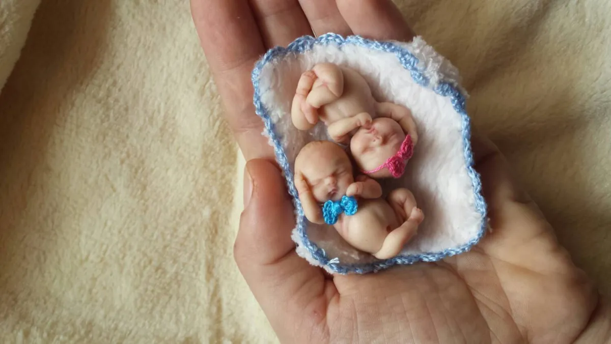 Two sleeping OOAK miniature baby dolls cuddled together in blue and white crocheted nest basket, held in palm - by Mini Baby Dolls