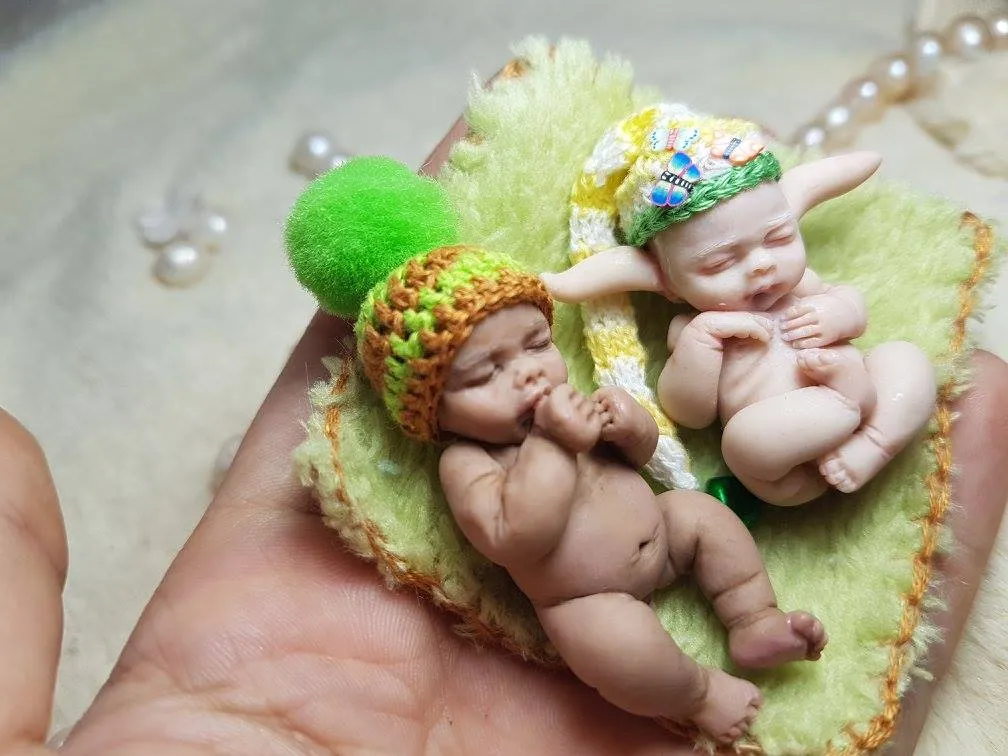 Two sleeping OOAK miniature baby dolls on green fuzzy blanket with colorful crocheted hats and green pom pom accessories - by Mini Baby Dolls