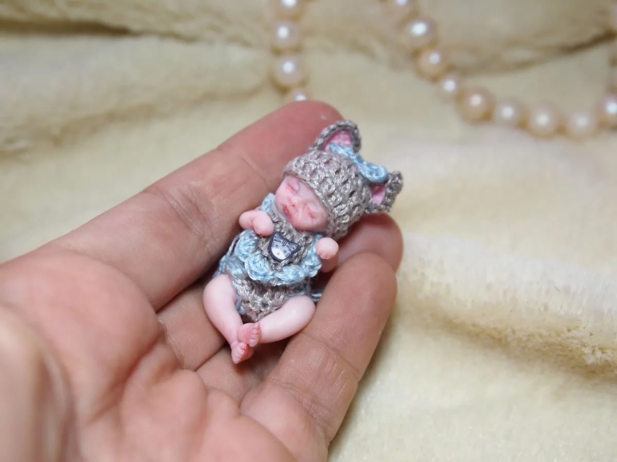 Sleeping OOAK miniature baby doll in grey crocheted elephant costume with pink trim, displayed in palm - by Mini Baby Dolls