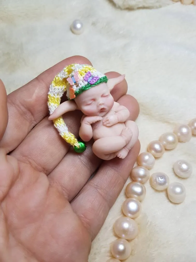 Sleeping OOAK miniature baby doll in colorful rainbow crocheted elf hat with pompom, held gently in palm with pearl beads - by Mini Baby Dolls