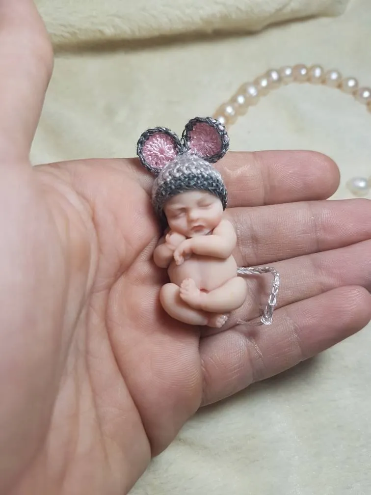 Sleeping OOAK miniature baby doll wearing a grey and pink crocheted mouse-ear hat, held gently in palm - by Mini Baby Dolls