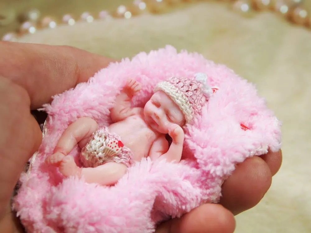 Sleeping OOAK miniature baby doll wearing a delicate gold crocheted crown, resting on fluffy pink blanket, displayed with pearl beads - by Mini Baby Dolls