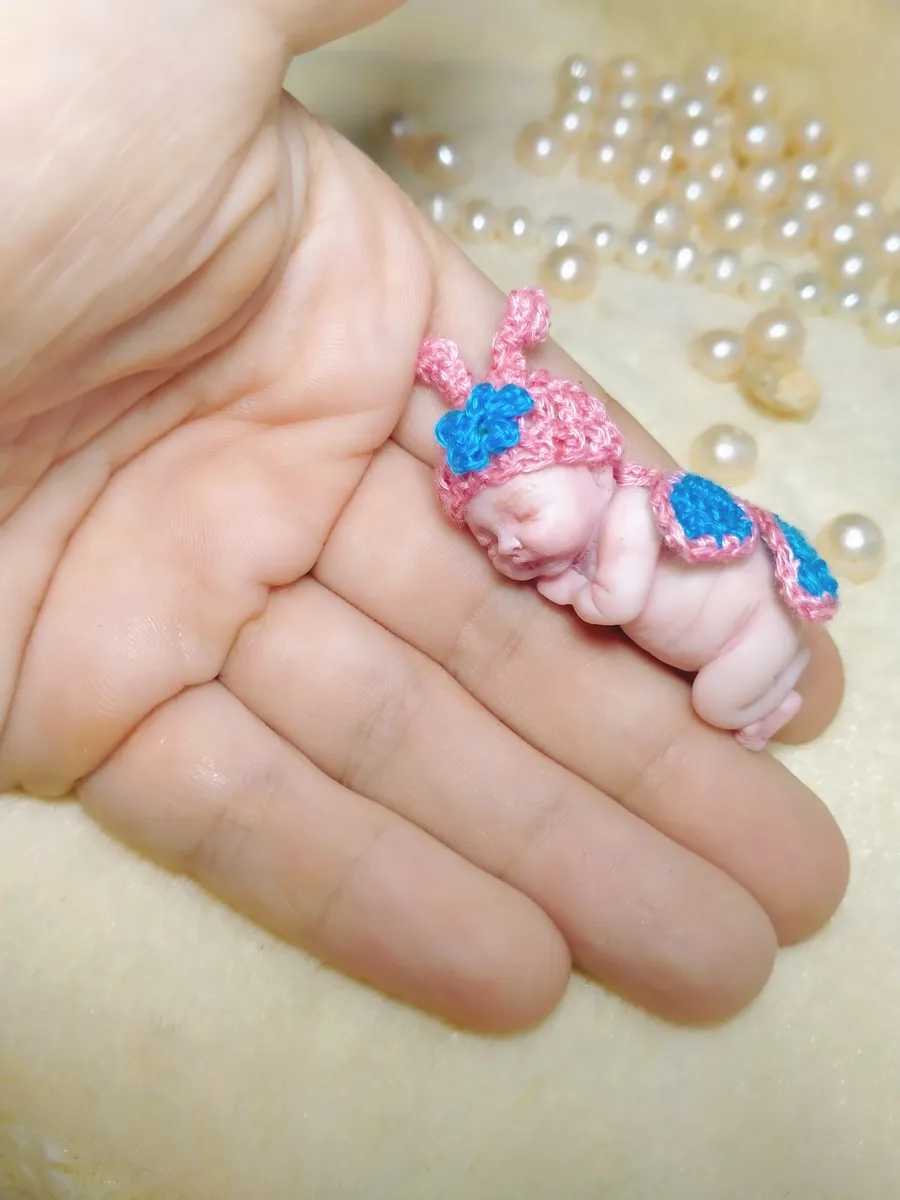 Two adorable OOAK miniature baby dolls snuggled together in palm wearing matching pink and blue crocheted bonnets - by Mini Baby Dolls