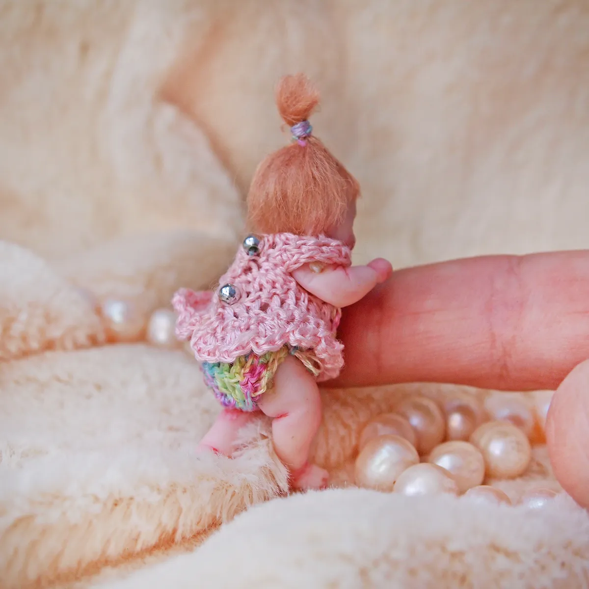 Standing OOAK miniature baby doll with red-ginger ponytail, wearing pink crocheted top with colorful rainbow bloomers, displayed with pearl beads on dark velvet - by Mini Baby Dolls