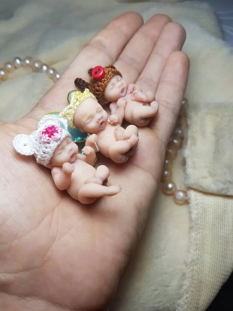 Three whimsical OOAK miniature baby dolls wearing colorful crocheted party hats in green, blue and purple, displayed together with pearl beads - by Mini Baby Dolls