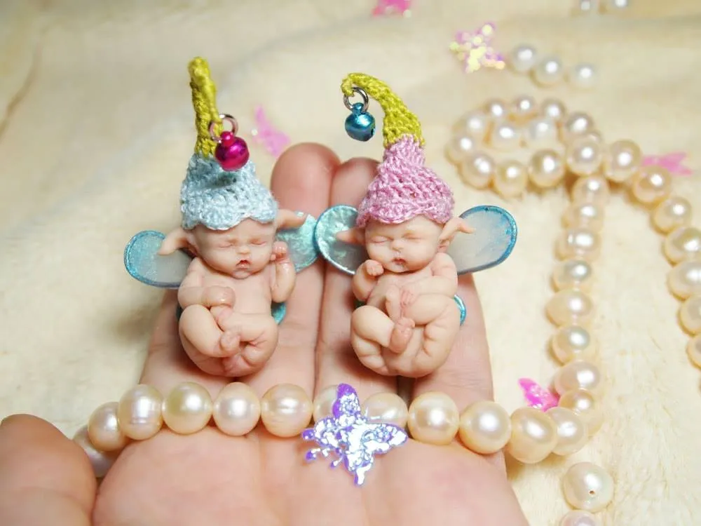 Two adorable OOAK miniature baby dolls in matching green crocheted frog costumes with big googly eyes, displayed together in palm - by Mini Baby Dolls