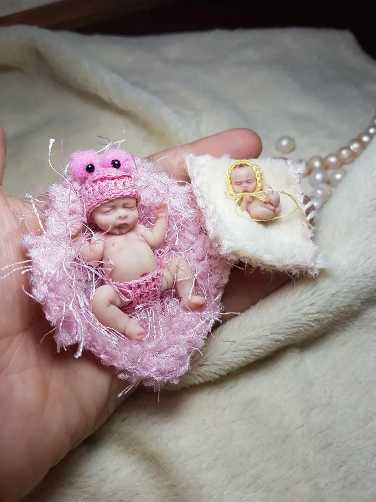 Two OOAK miniature baby dolls in pink fuzzy nest - one on white pillow, one in pink frog costume, displayed as adorable pair - by Mini Baby Dolls