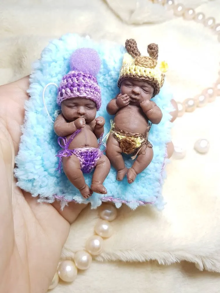 Two OOAK miniature baby dolls on blue fluffy pillow - one in purple crocheted outfit with pink hat, one in gold diaper with bunny ear hat - by Mini Baby Dolls