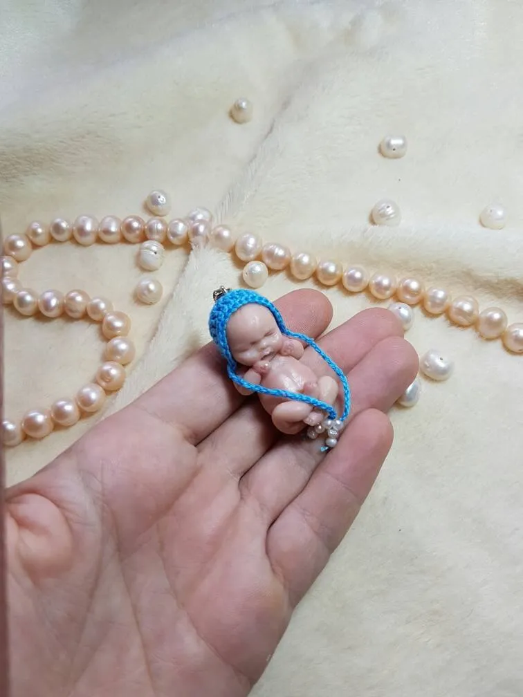 Ultra-tiny sleeping OOAK miniature baby doll in bright blue crocheted outfit with matching bonnet, held gently in palm to show miniature scale, with pearl beads - by Mini Baby Dolls