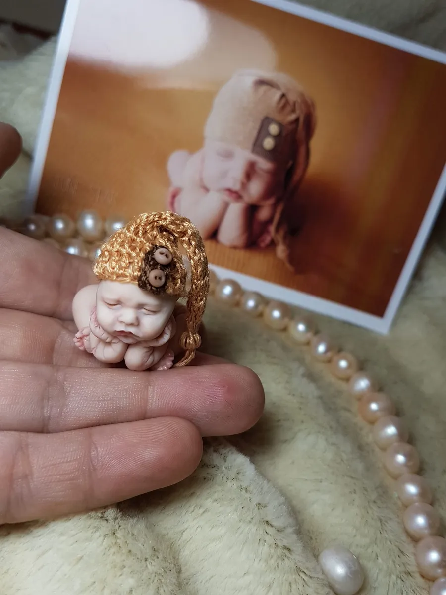 Sleeping OOAK miniature baby doll wearing vintage gold crocheted bonnet with flower detail, displayed with printed photo in background - by Mini Baby Dolls