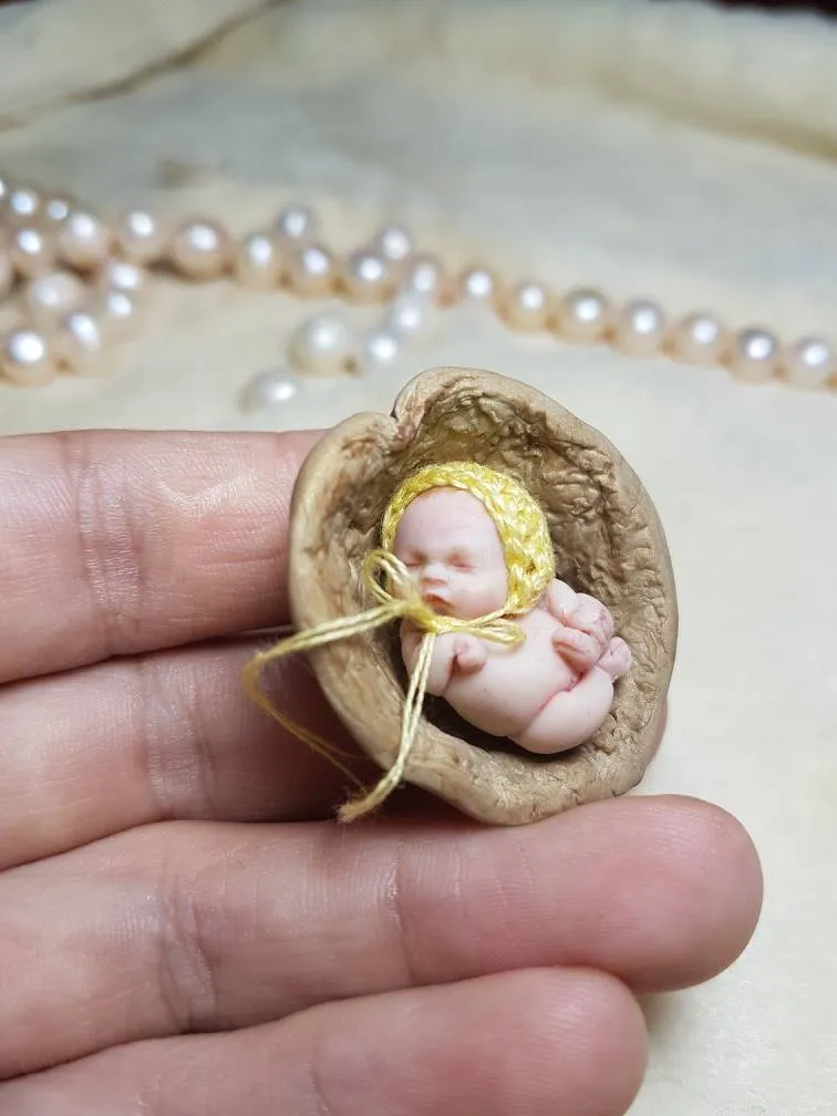 Enchanting OOAK miniature baby doll sleeping peacefully in a walnut shell cradle, wearing a yellow crocheted bonnet with ribbon ties - by Mini Baby Dolls
