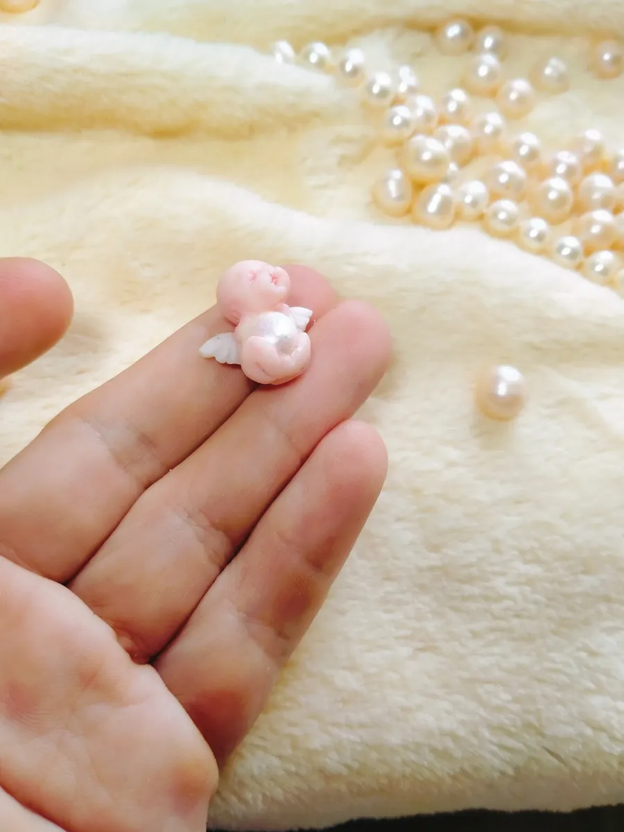 Ultra tiny OOAK miniature baby doll in white held on fingertip with single pearl bead for scale, showing incredible miniature craftsmanship - by Mini Baby Dolls
